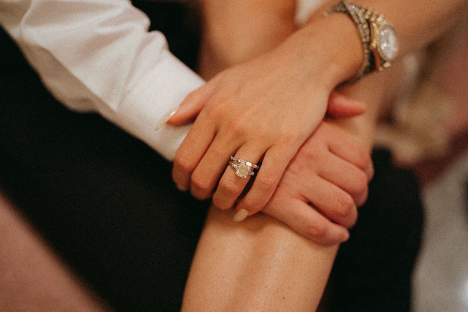 Close-up of a couple holding hands, showcasing a stunning diamond engagement ring on the woman's finger.