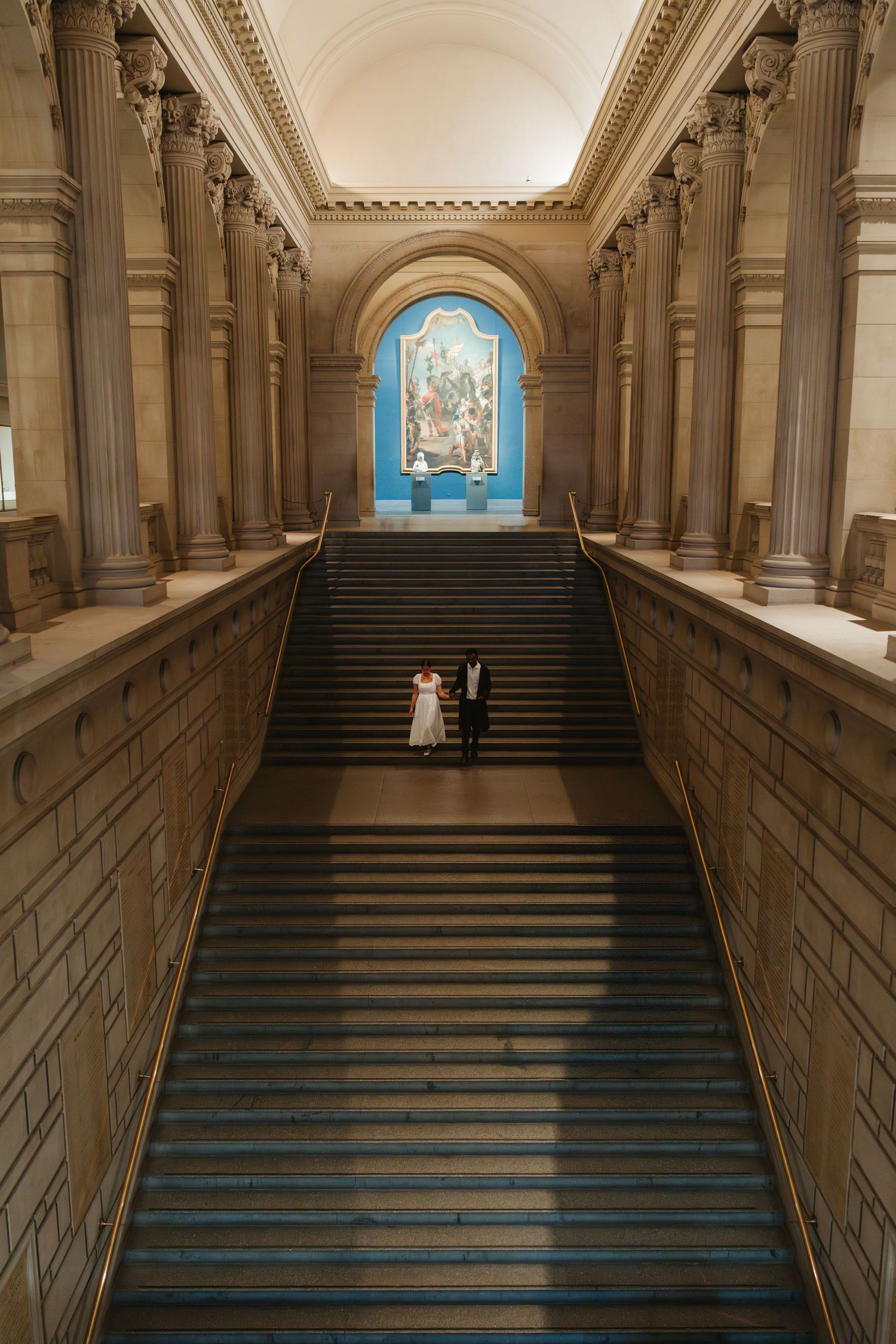 A silhouetted couple viewed through classical architecture in a museum setting.
