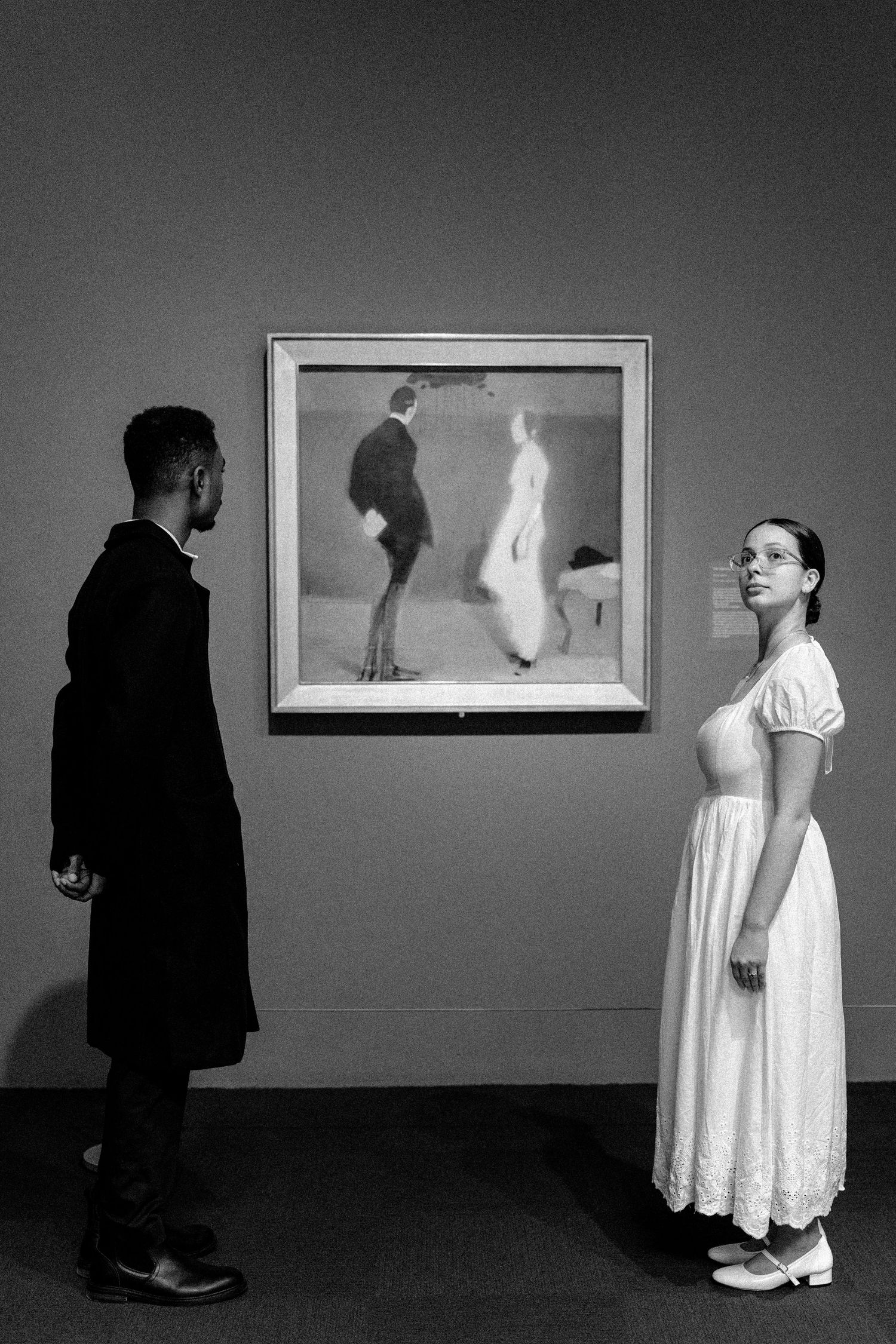 Black and white photo of a man and woman viewing a framed painting in an art gallery museum.