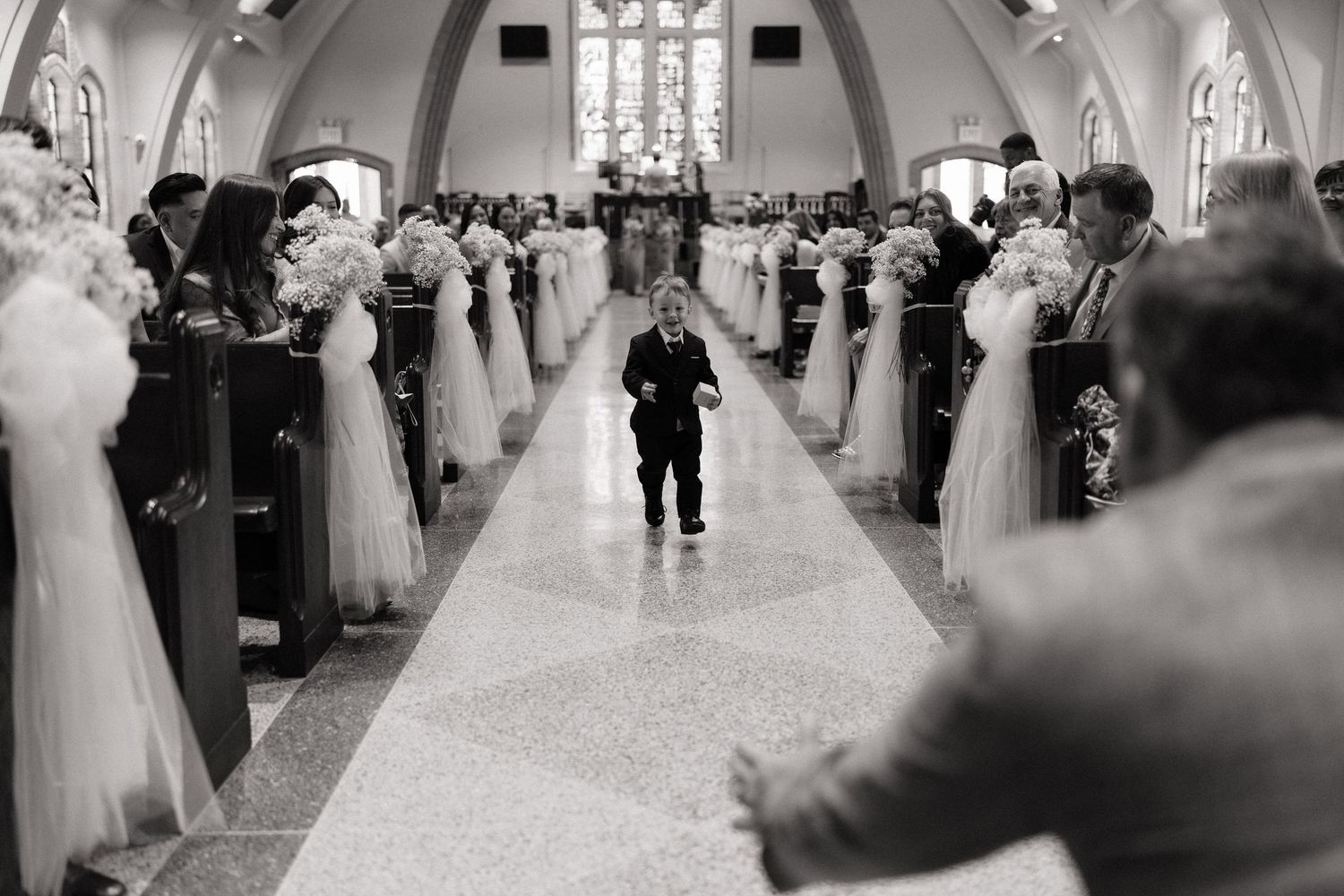 A young ring bearer walks down the church aisle at a wedding ceremony in black and white photo.
