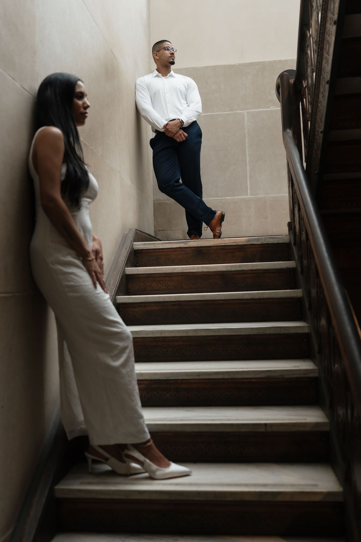 Couple ascending elegant stone staircase in formal attire.