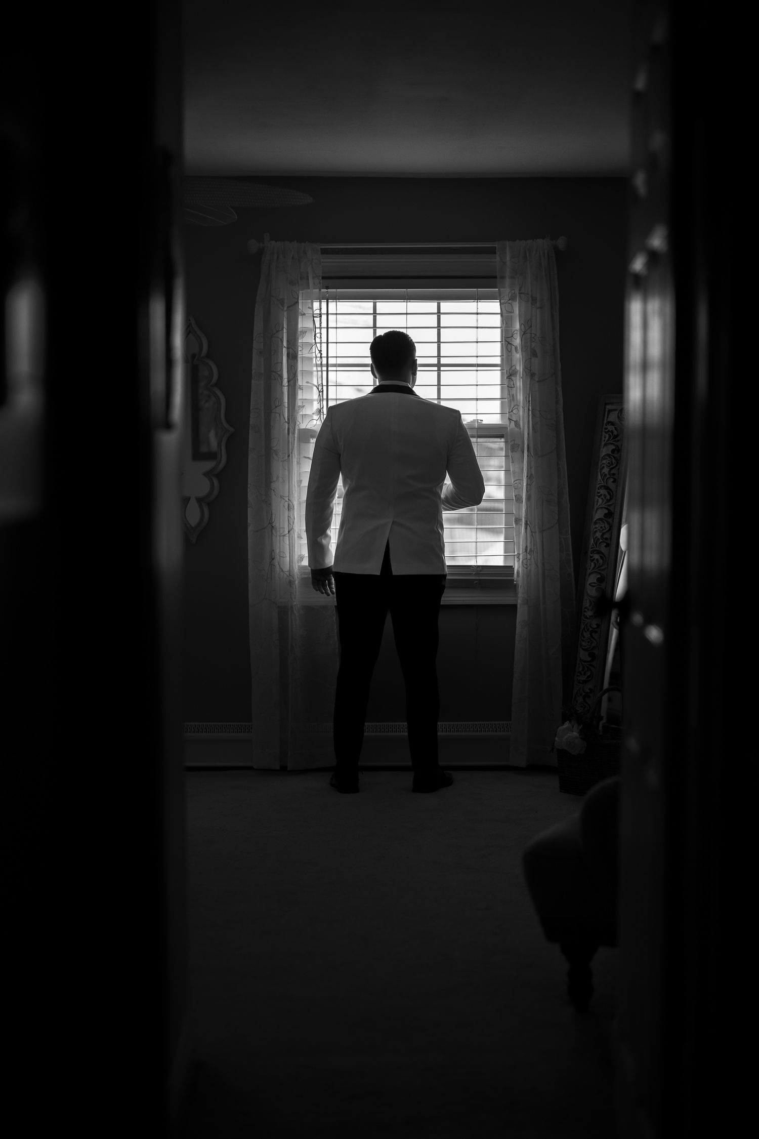 A dark silhouette of a person standing by a window in a dimly lit hallway creates a moody, noir atmosphere.