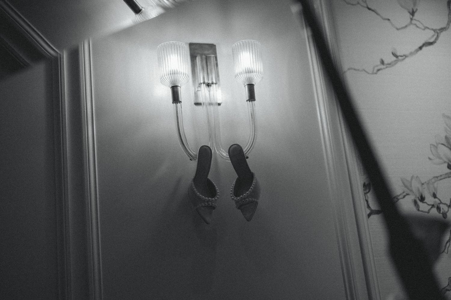 Black and white photo of elegant strappy heels hanging on a wall sconce with glowing candle lights.