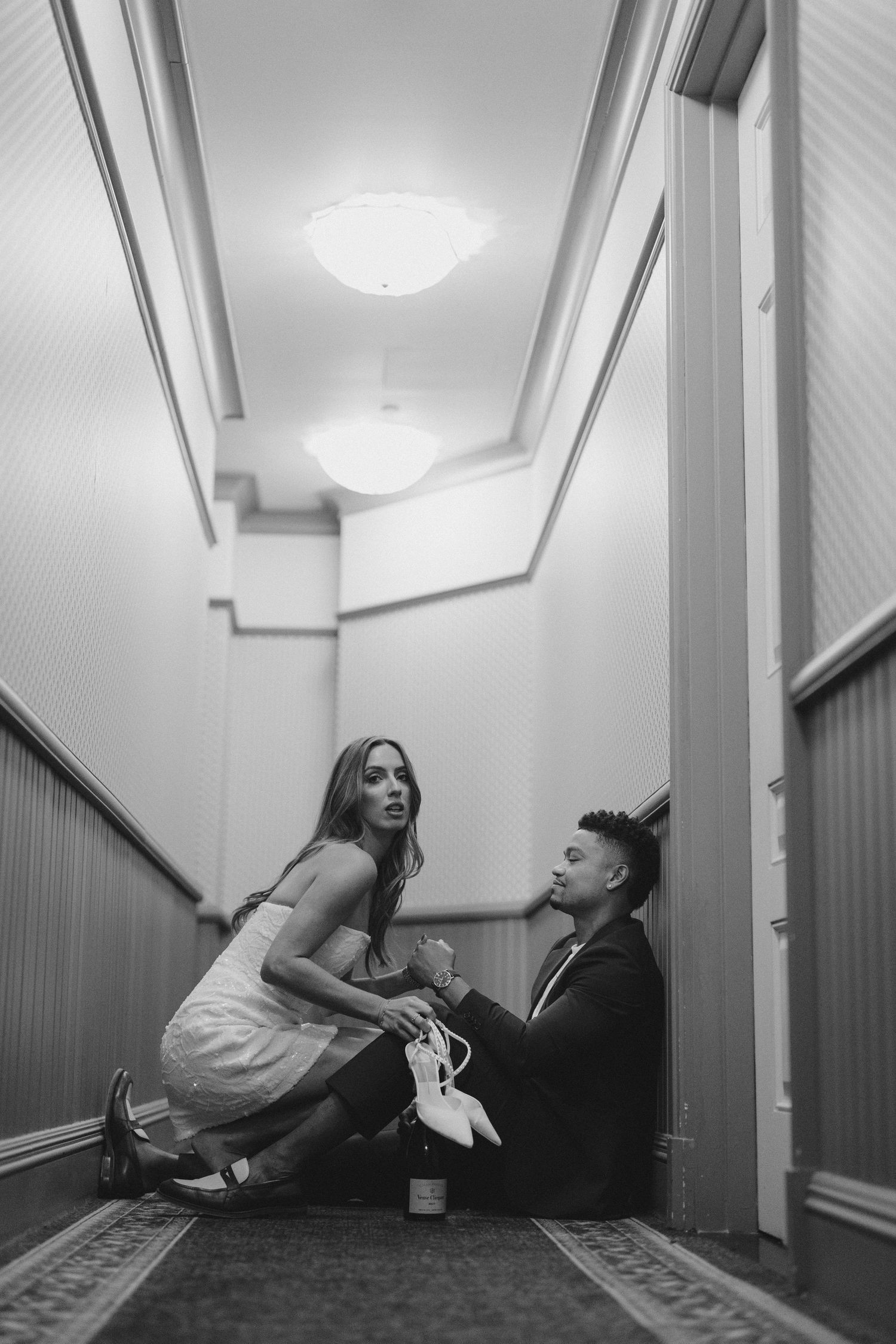 Couple relaxes in intimate poses along hallway floor in black and white.