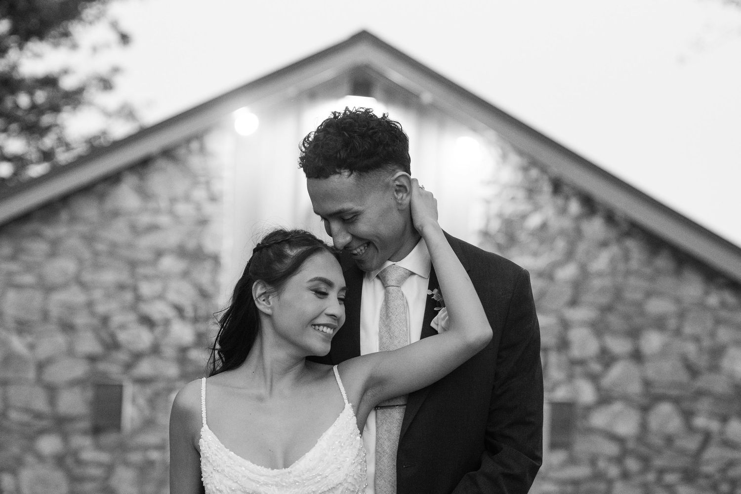 Romantic wedding couple poses against stone building during sunset.