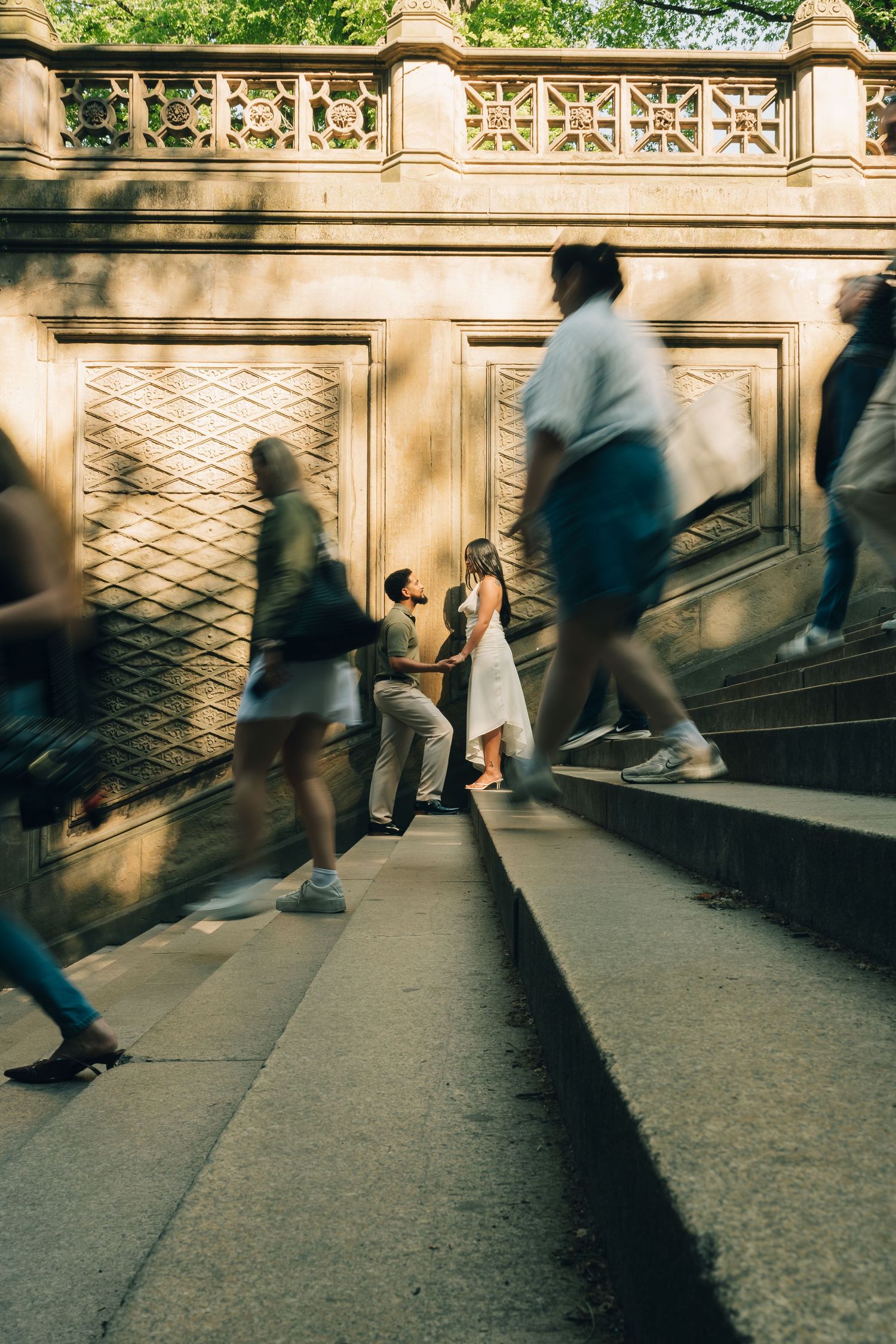 Couple sharing a romantic moment at Bethesda Terrace in Central Park, NYC, surrounded by blurred pedestrians.