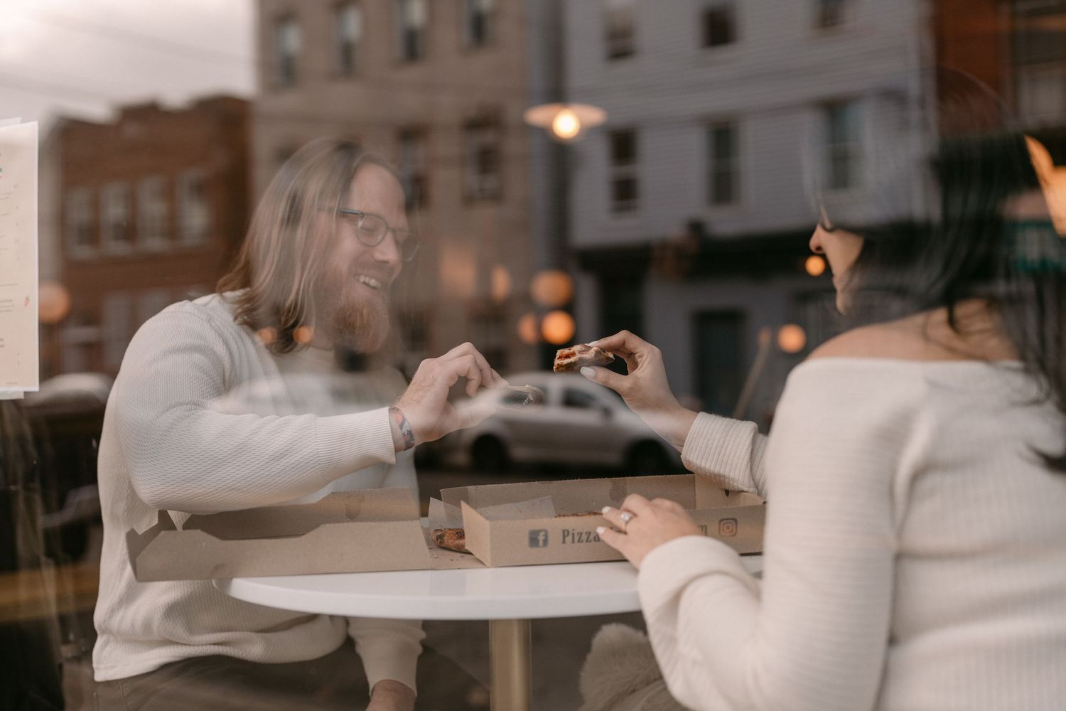 Couple sitting at cafe table seen through window reflection.