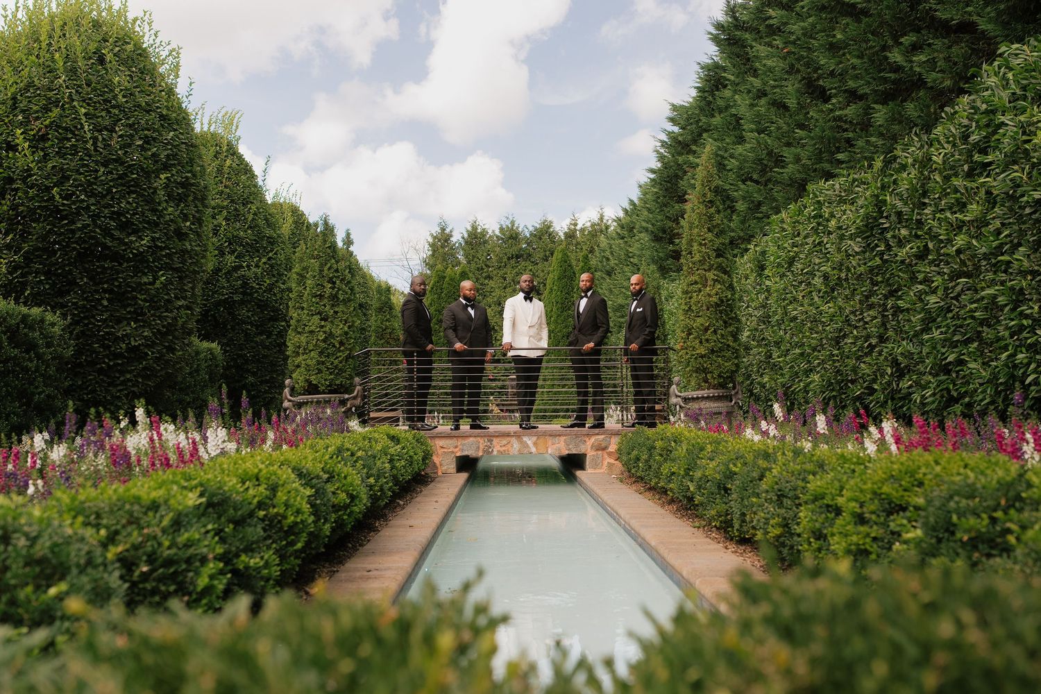 A serene garden path lined with tall manicured hedges leads to a classical building in the distance.