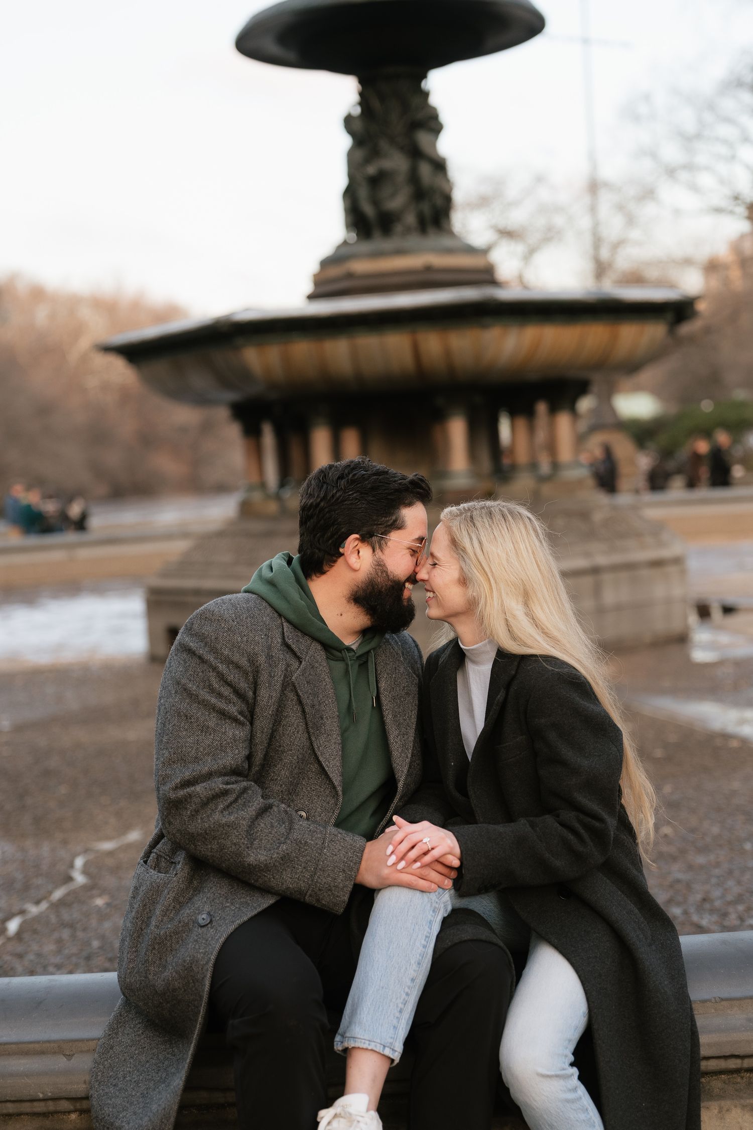 Couple sharing a romantic kiss while sitting by Bethesda Fountain in Central Park on a cool autumn day.