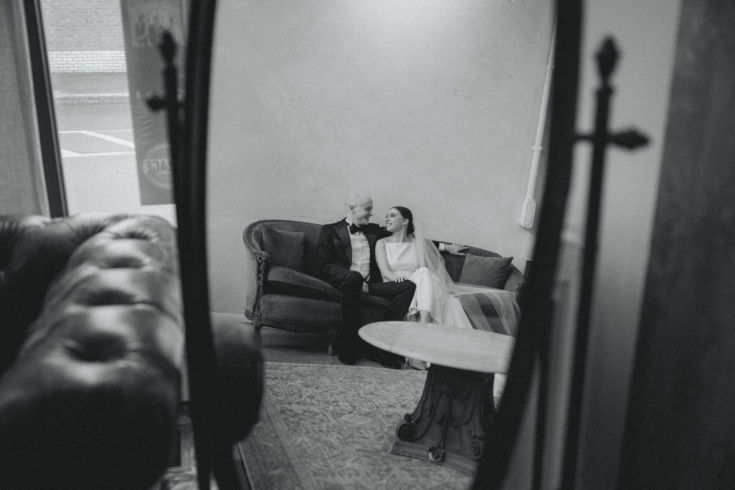 Black and white photo of a couple sharing a romantic moment on a couch, reflected in a mirror.