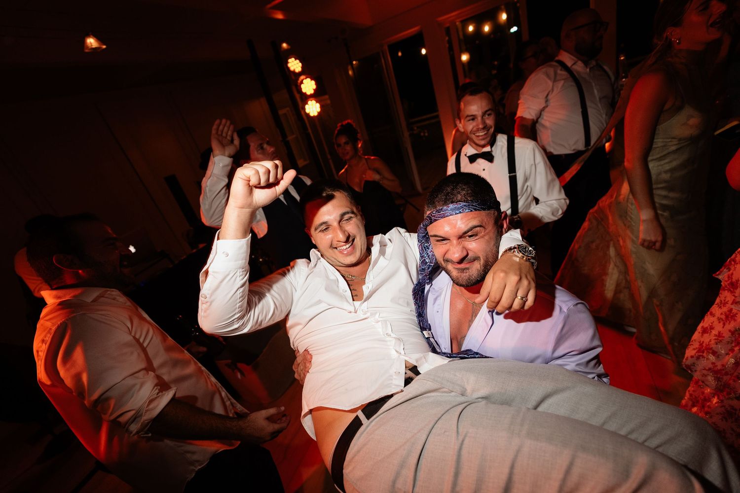 Two men smiling and celebrating at a wedding reception dance floor, dressed in white shirts.
