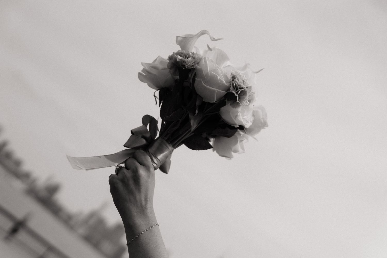 A hand holding a bouquet of roses up in the air in a black and white photo.