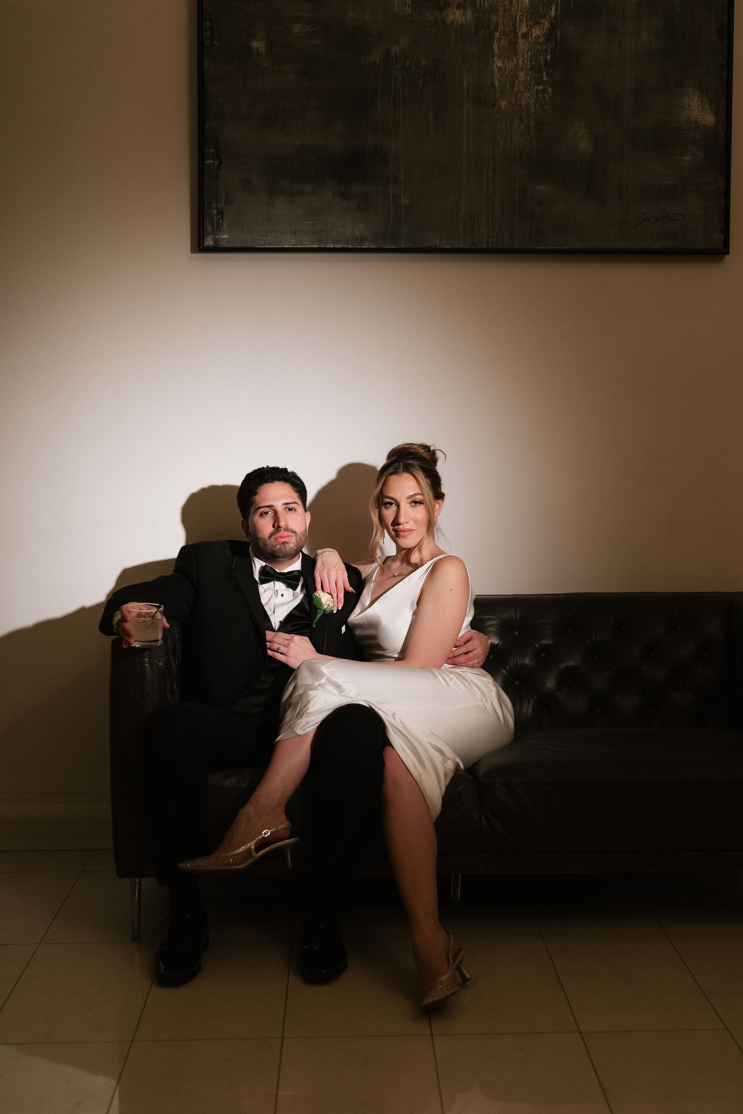A couple relaxes on a dark leather couch in a moody, intimate setting.