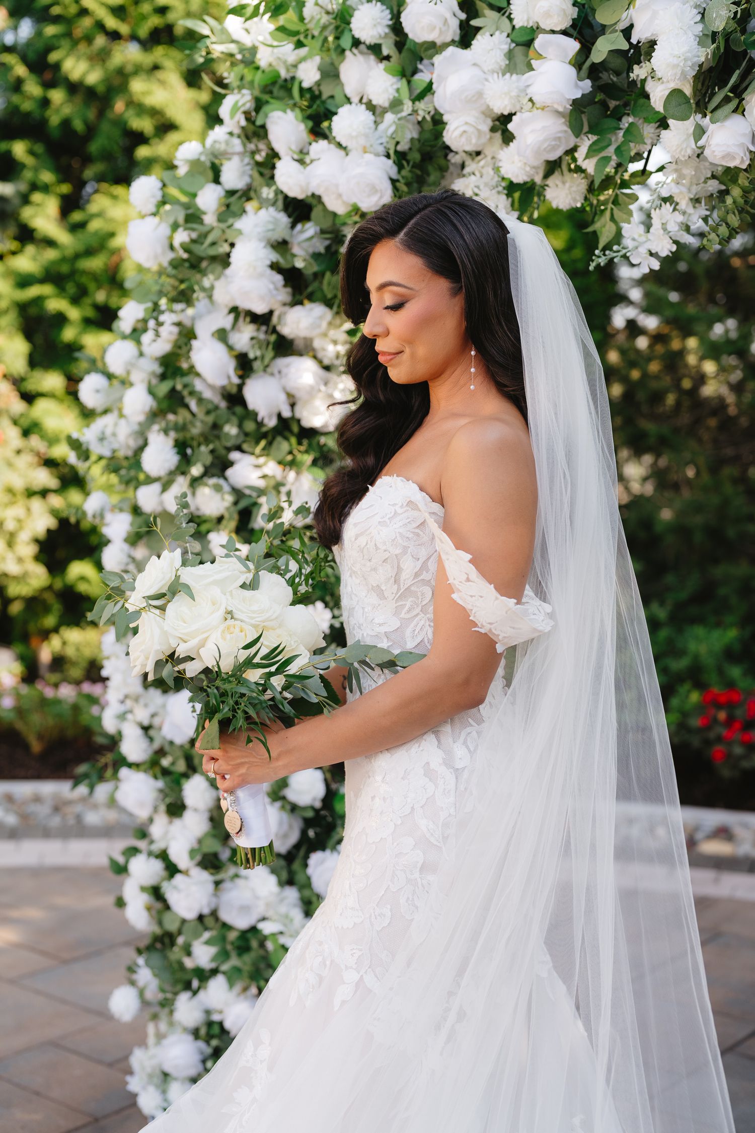 Bridal portraits against white floral arch with cascading roses and greenery.