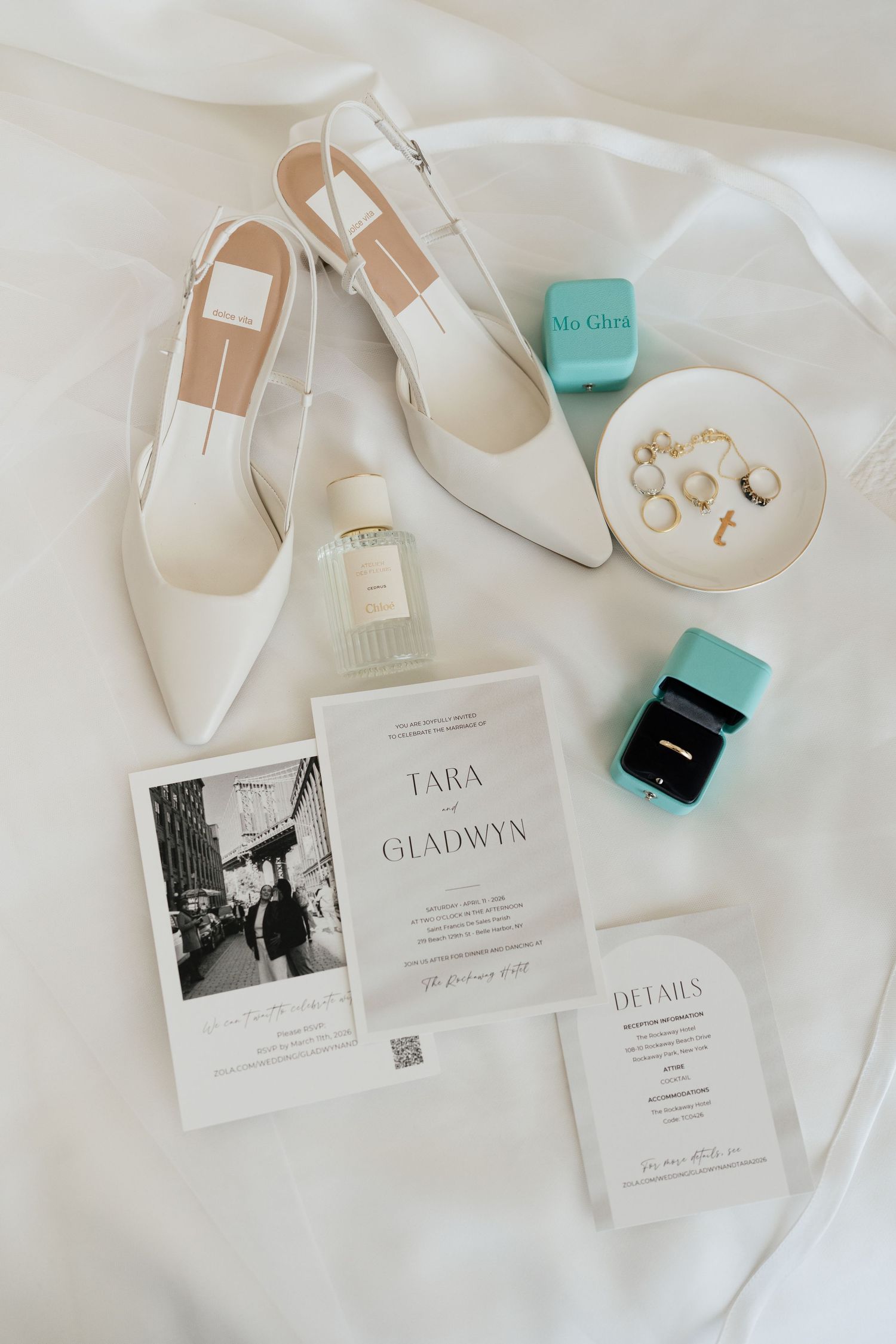 Elegant wedding flat lay with white heels, Tiffany blue boxes, gold rings, perfume, and Tara & Gladwyn wedding invitations.