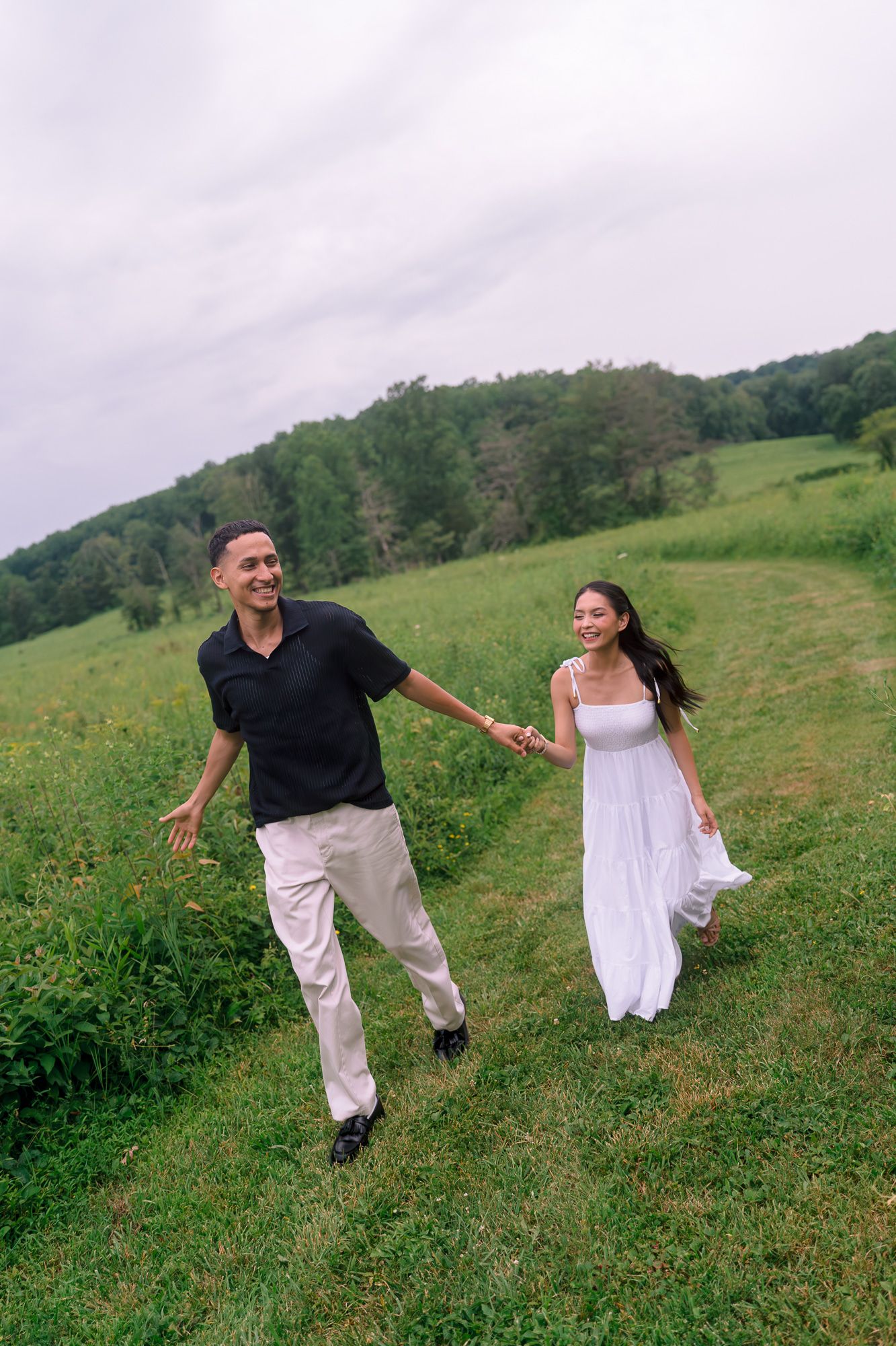 Couple running playfully through a green hillside meadow.