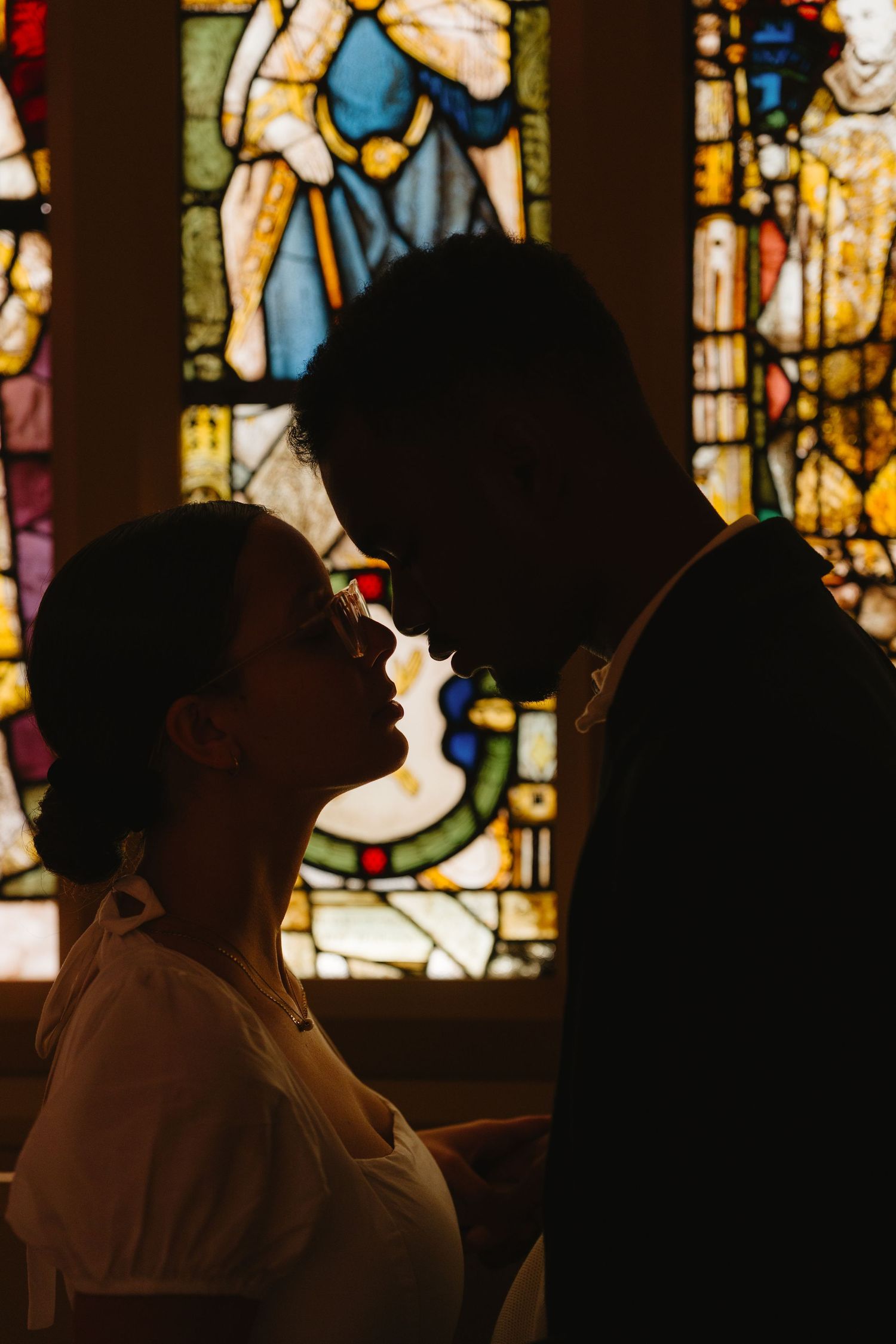 A romantic silhouette of a couple against colorful stained glass windows in a church setting.