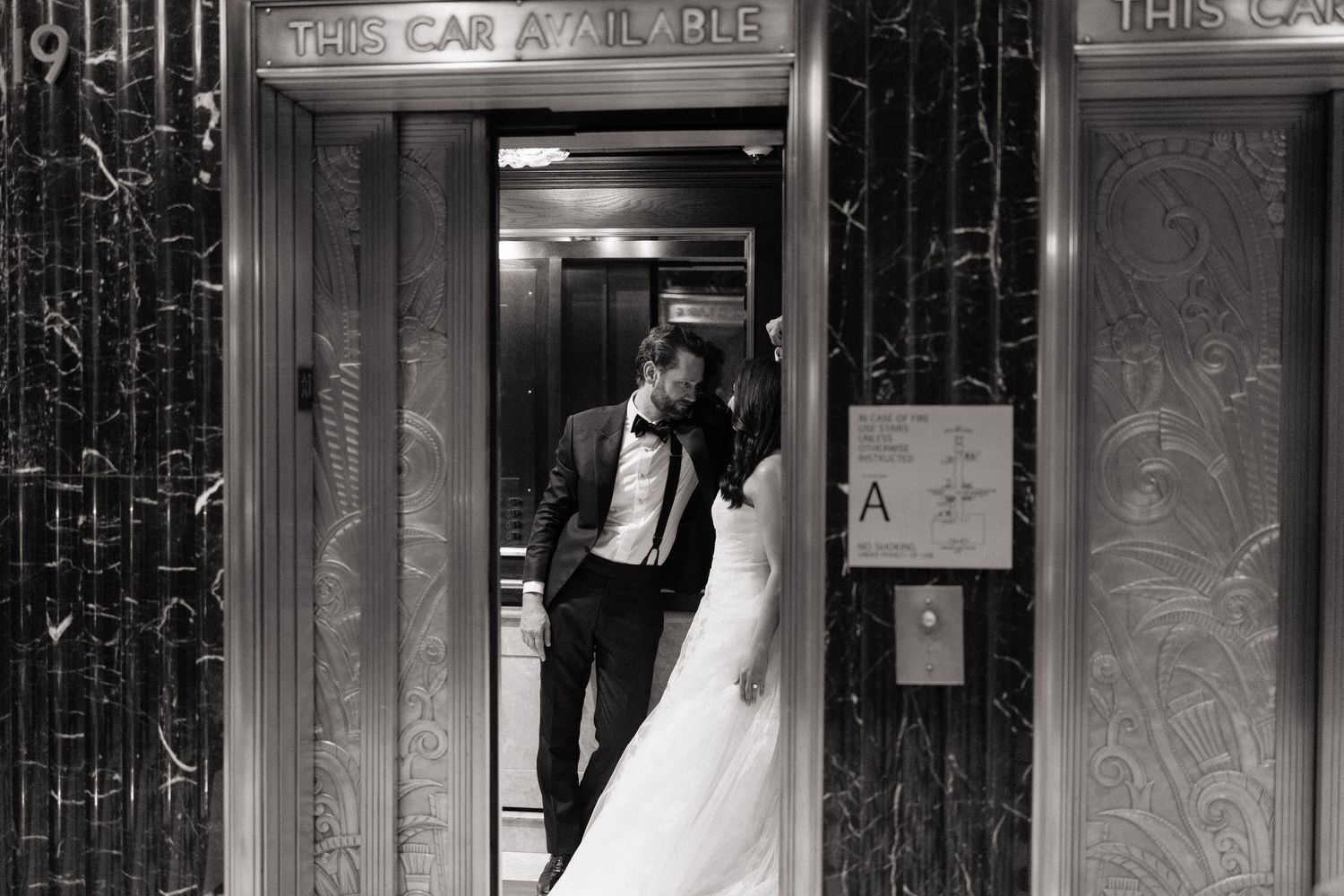 Black and white photo of bride and groom sharing a kiss in an elegant elevator doorway on their wedding day.