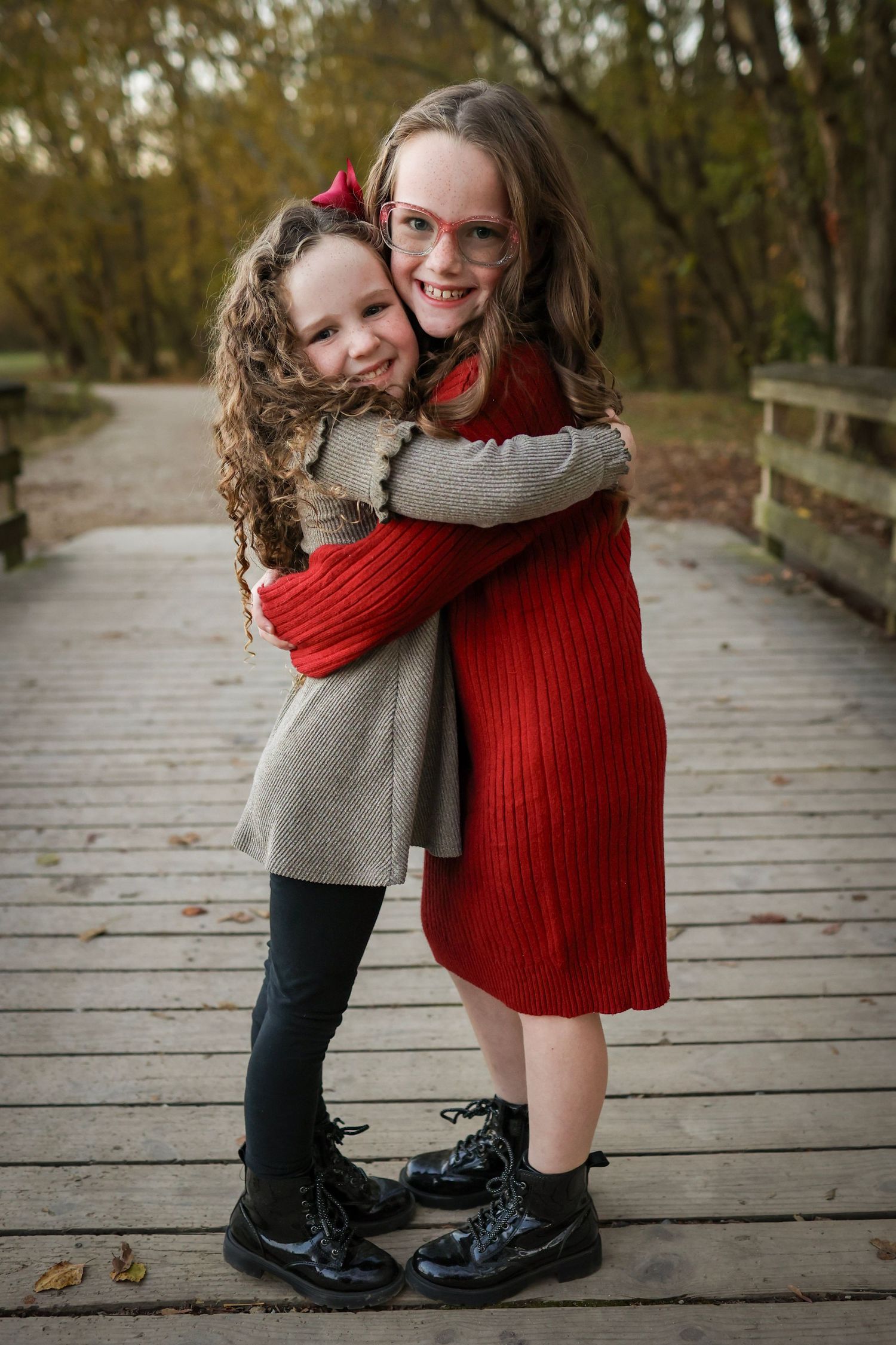 Two sisters hugging on the bridge at McAlpine Park during a professional sibling portrait session.