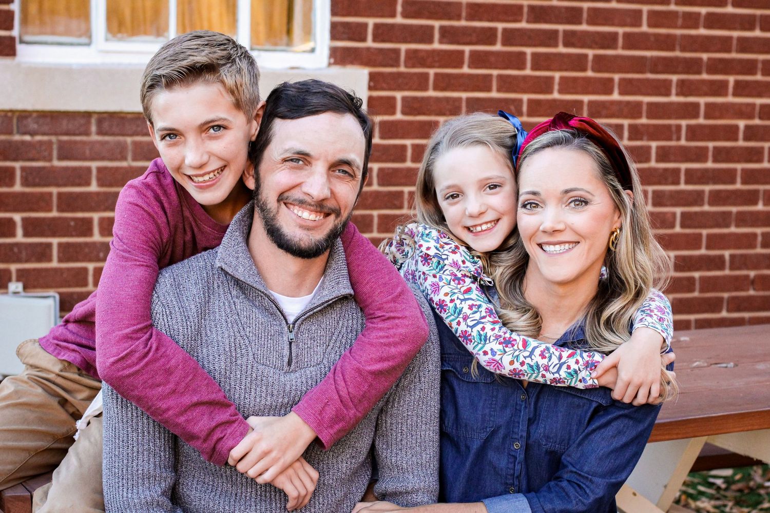 Family of four hugging and smiling during an outdoor session in Monroe, NC.
