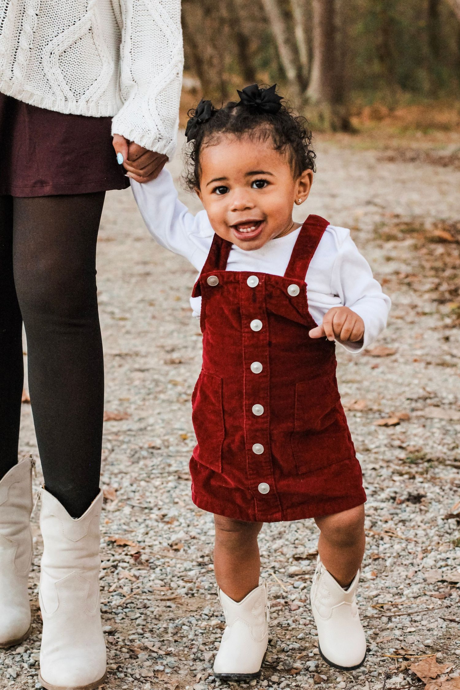 Toddler holding her parent's hand and smiling during a park photo session.