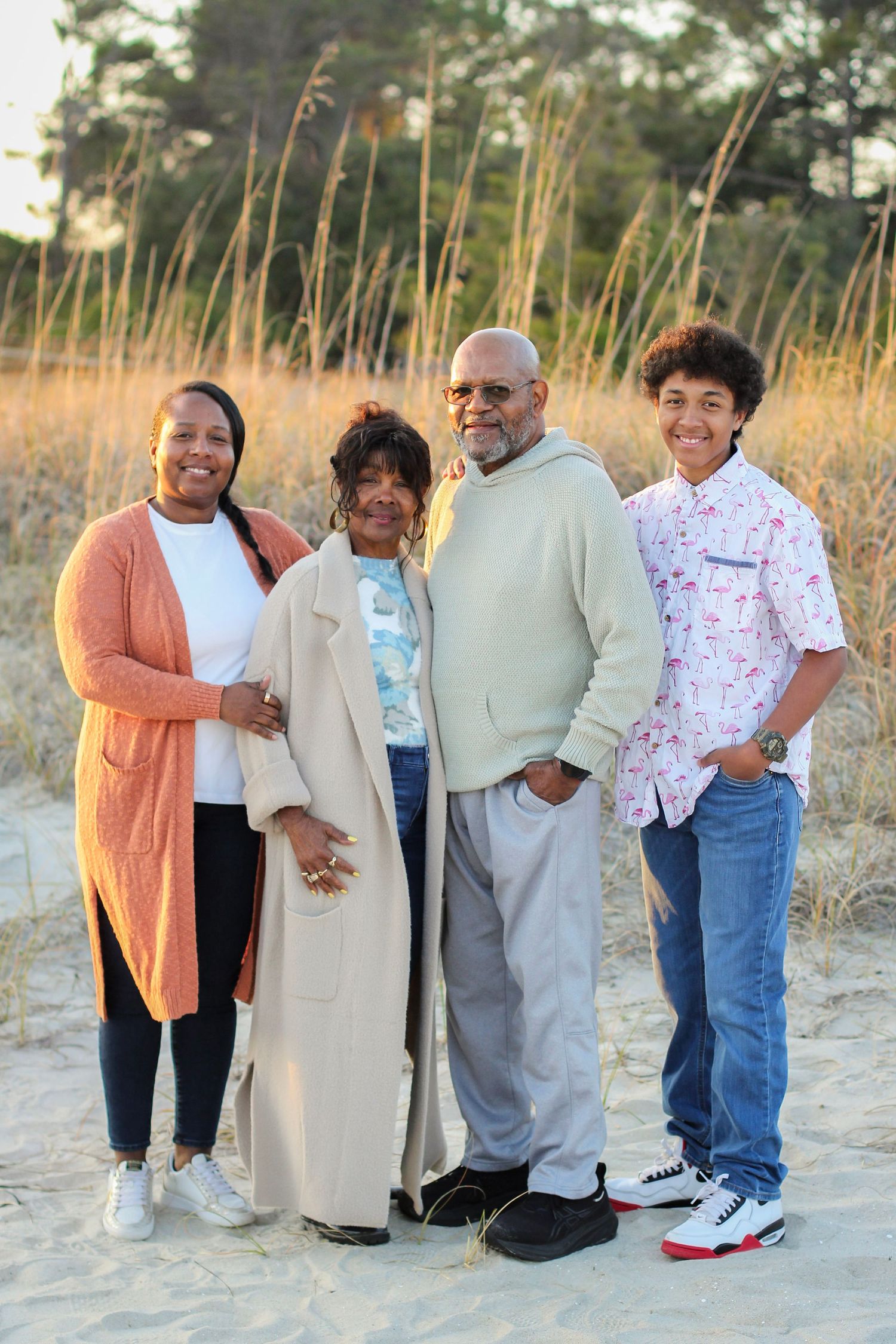 Family of four posed on the beach looking at the camera for summer portraits.
