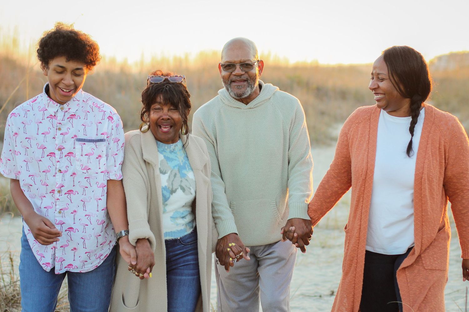 Family of four walking and laughing together on the beach during a sunset session.