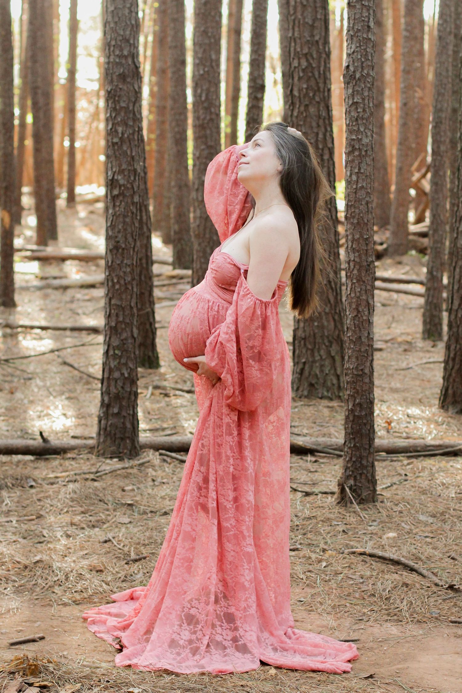 Whimsical maternity photo of a pregnant woman standing among the trees in a forest setting.