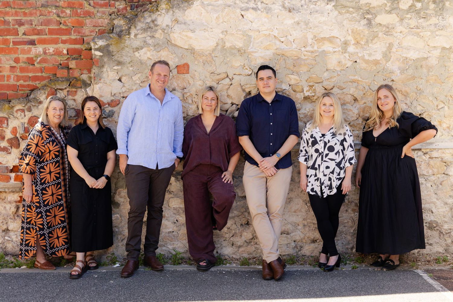 Group of people sitting casually against rustic brick and stone wall backgrounds in coordinated outfits.