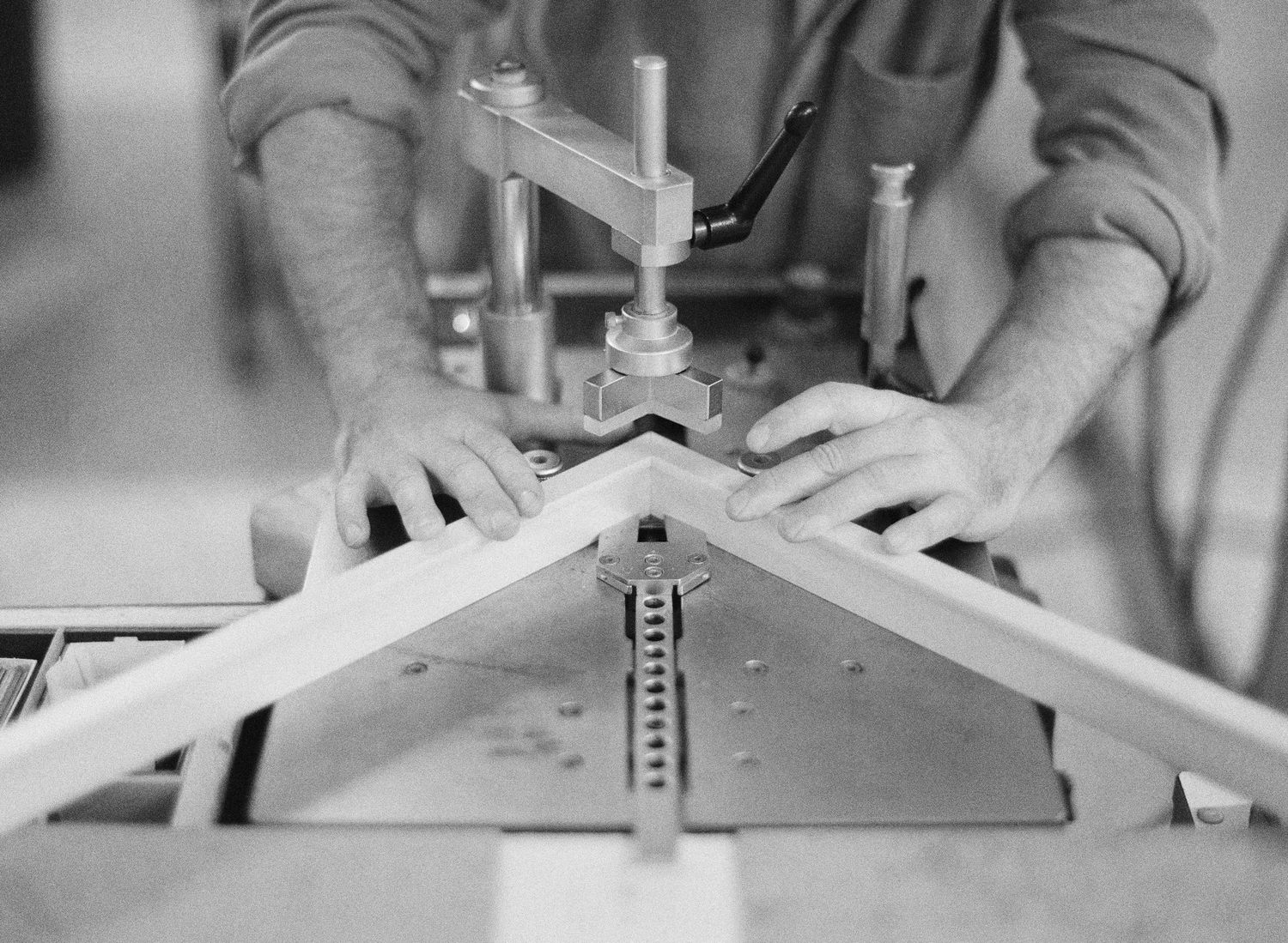Close-up black and white image of hands working with tools on a construction or crafting project.