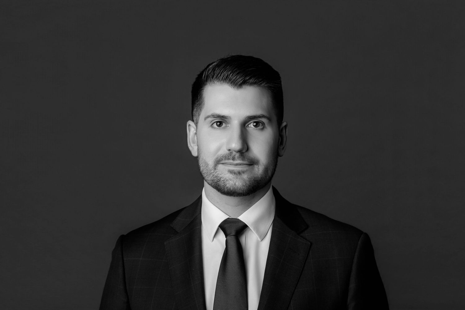 Professional black and white headshot portrait of a businessman in a dark suit against a gray background.