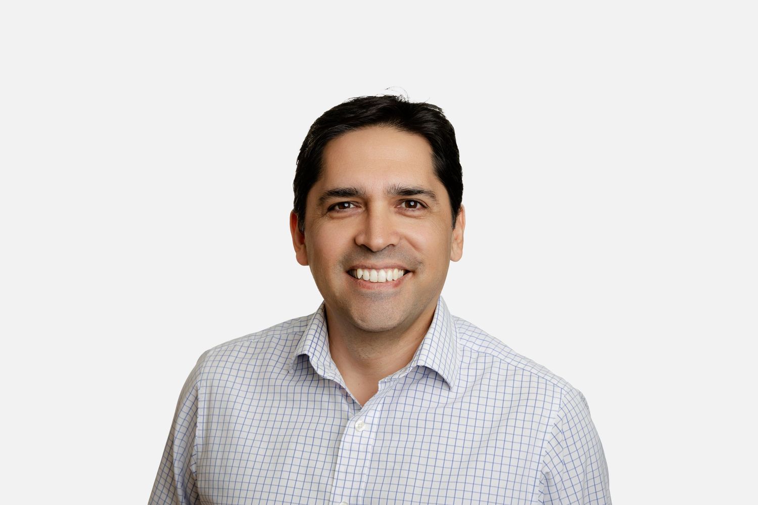 Professional wearing a light checkered button-down shirt smiles warmly against a white background.