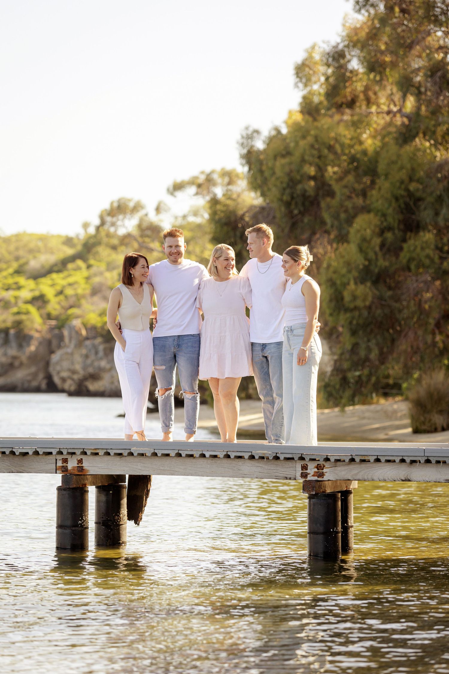 Family wearing white outfits walks together on wooden pier by lake during golden sunset.