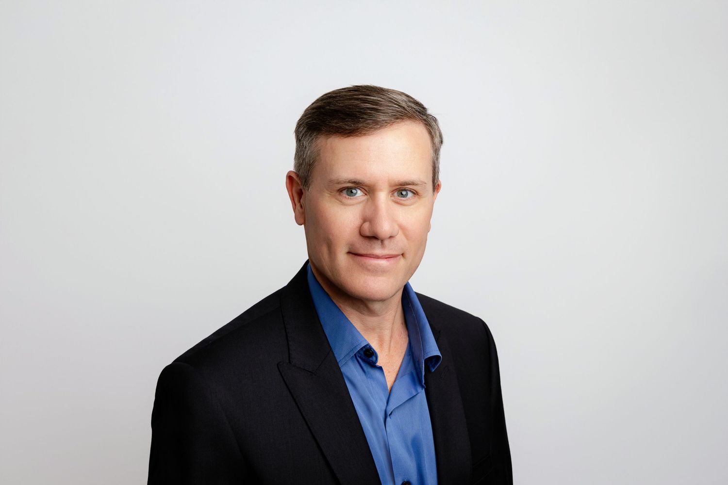 Professional headshot of a person wearing a dark suit jacket and blue shirt against a light background.