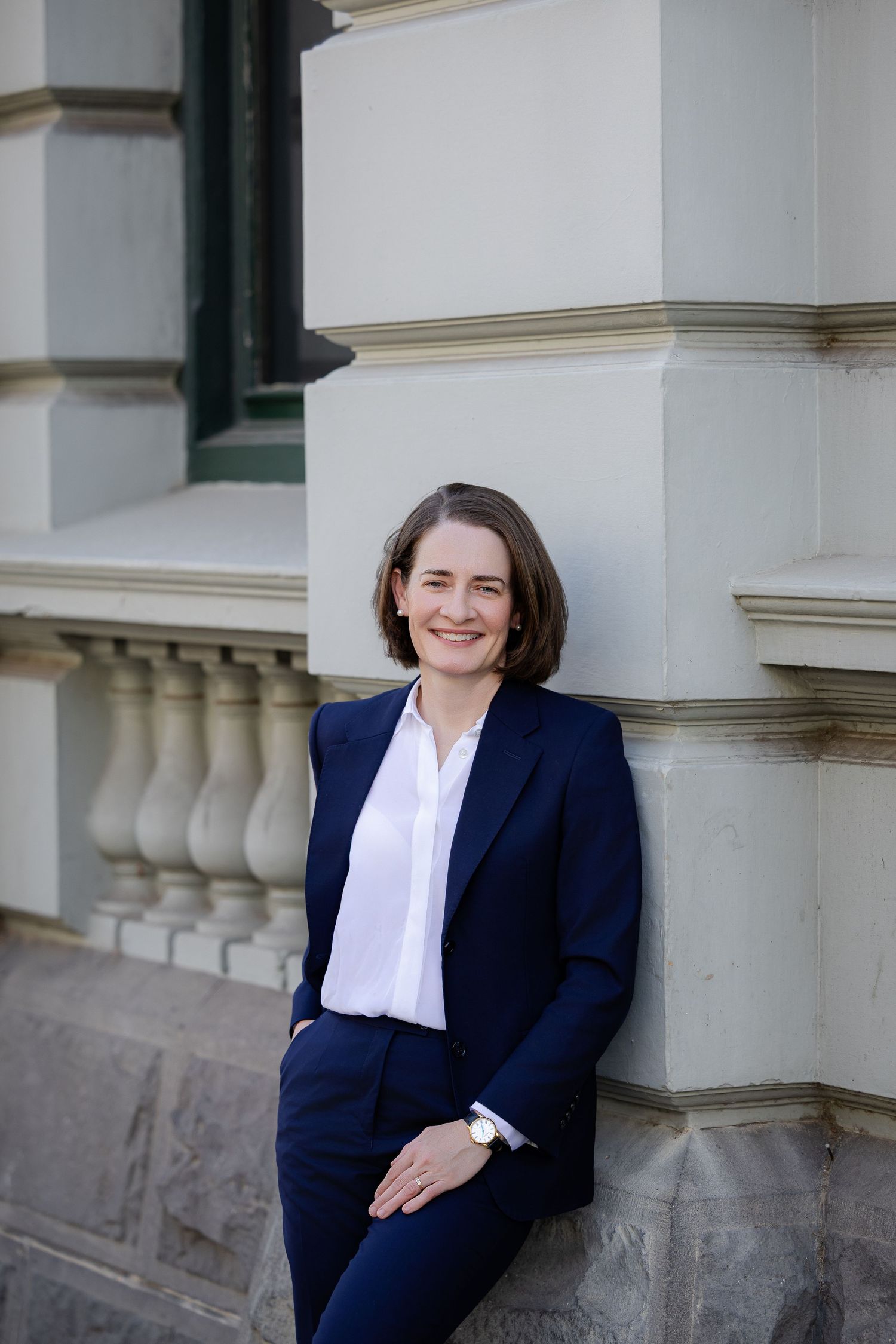 Professional woman in navy suit smiling confidently against classical building exterior.