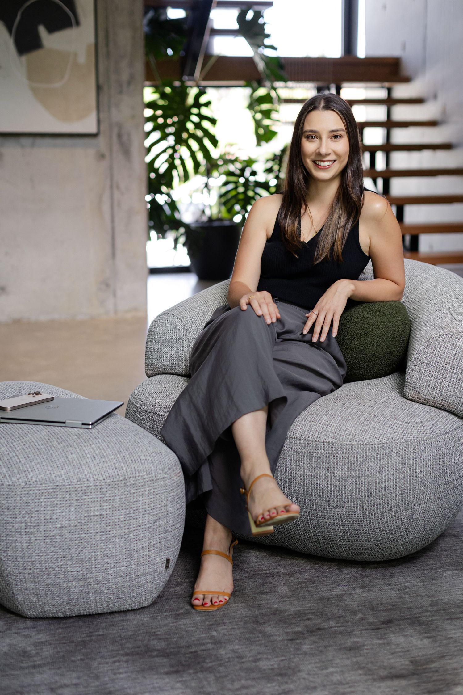 Person relaxing on modern gray bean bag chair in contemporary living space with dark flooring and indoor plants.