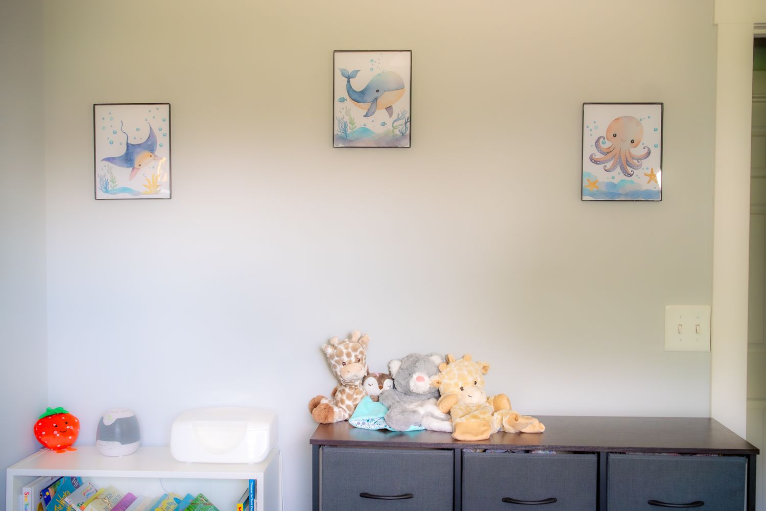 Plush stuffed animals and toys displayed on white shelves against a beige wall in a cozy nursery setting.