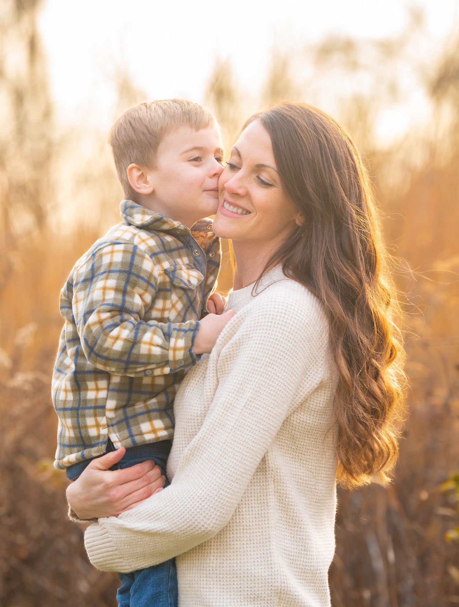 A tender moment between parent and child is captured in golden sunlight during an outdoor portrait session. Quad Cities Photographer