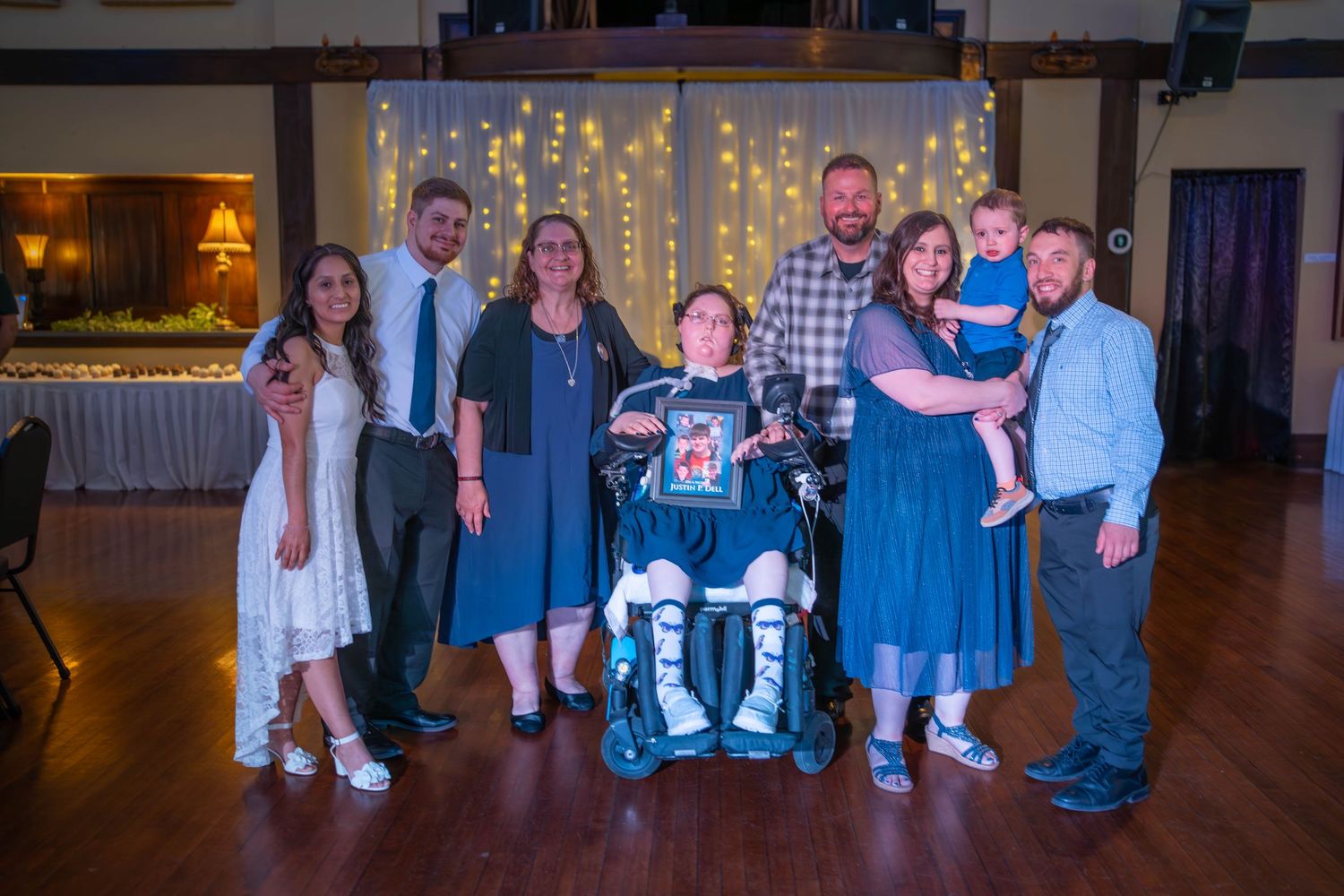 Group of people in formal attire posing together at a party venue with string lights in the background. Wedding Quad Cities Photography