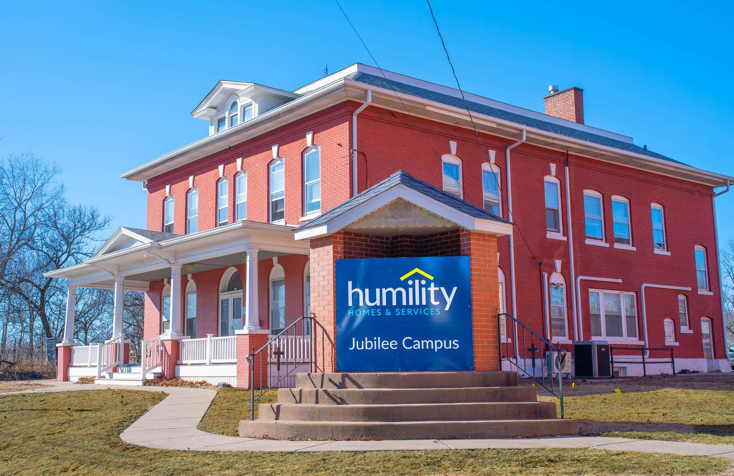 A red brick building with white trim and columns displaying a Humility Homes Jubilee Campus sign. Quad Cities Photography