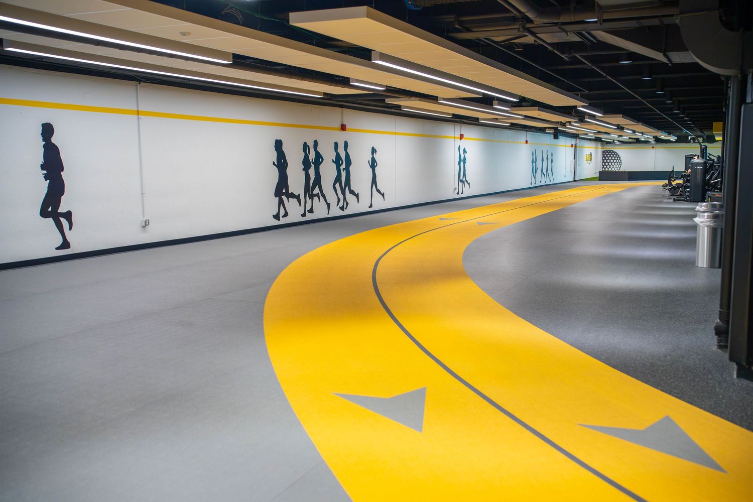 Black Hawk College Hawks Nest. Modern indoor running track with yellow lane markings and silhouette runner wall art in a fitness facility.