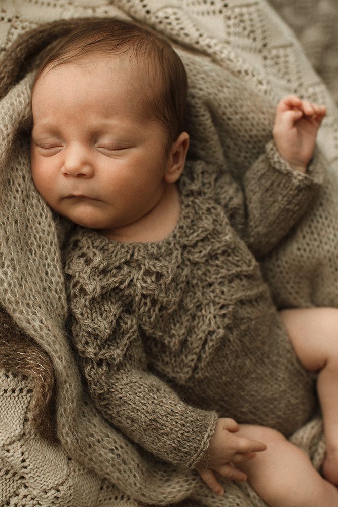 Lancashire newborn photographer. A sleeping baby wearing a cozy gray knit sweater lies peacefully on soft textured fabric.