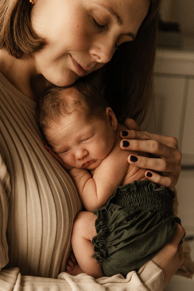 A mother tenderly holds her sleeping newborn baby dressed in green, sharing a peaceful bonding moment.