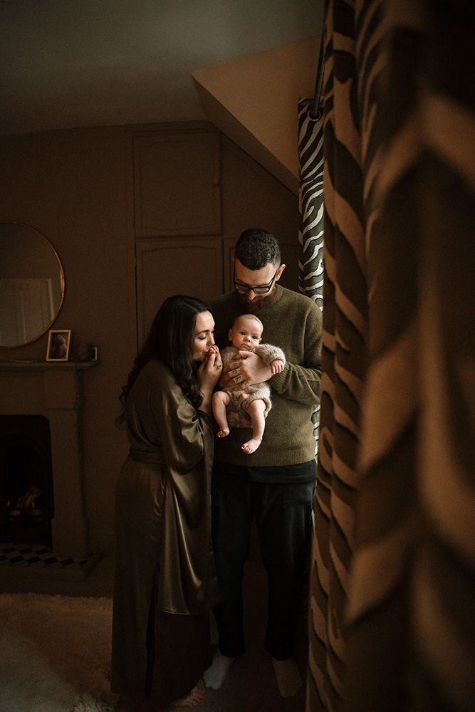 A black and white photograph showing tender moments between a parent and baby in low light. Captured on a newborn photoshoot in Manchester.