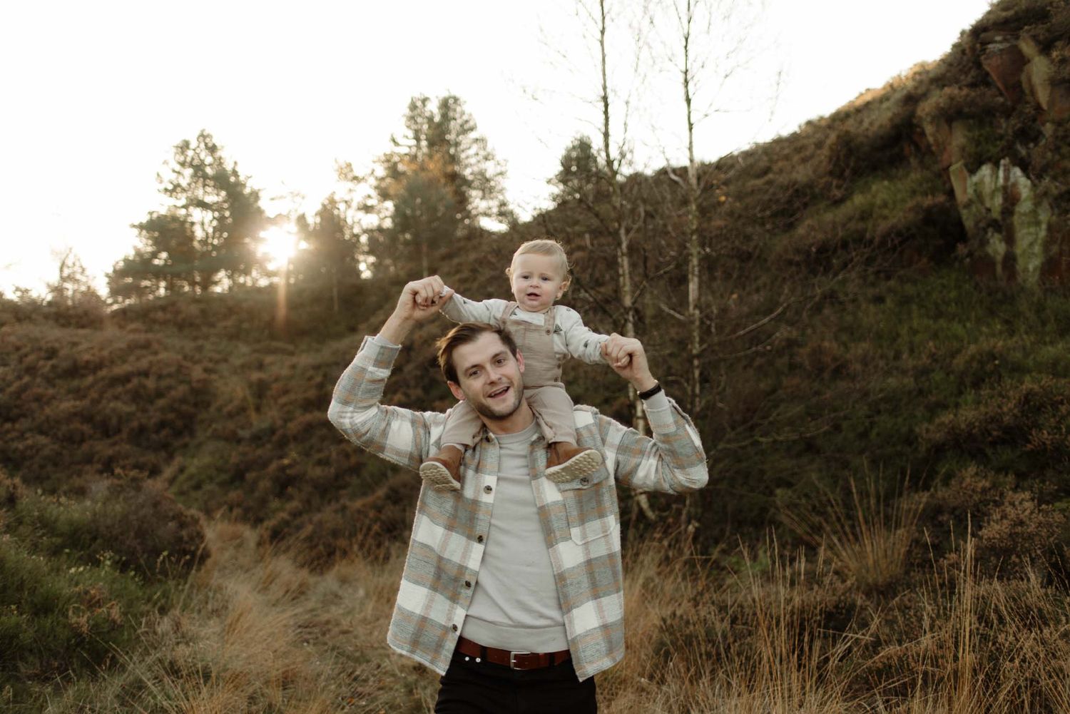 A sunset scene in the mountains with people posed joyfully together among brown grassy slopes and evergreen trees.