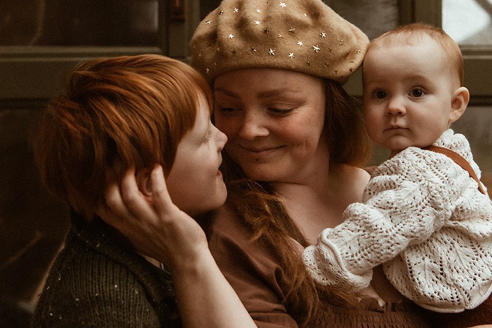 Lancashire motherhood photographer. A warm family moment shows a parent wearing a beret embracing two young children in cosy knit sweaters.