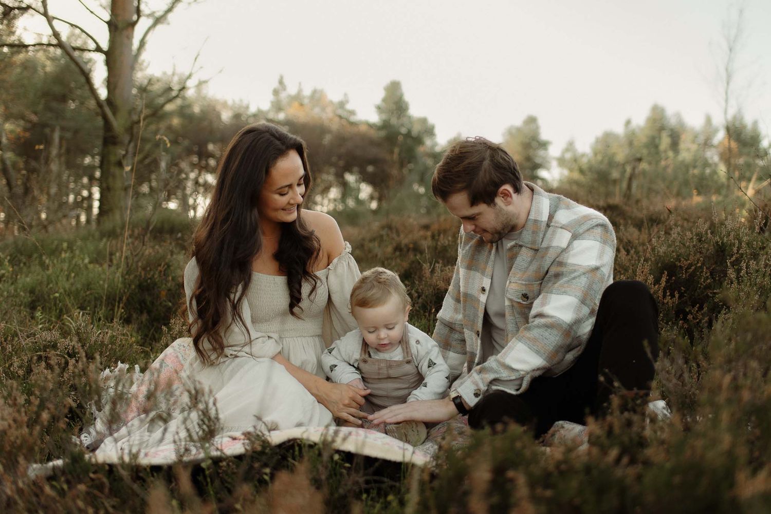 Family sitting together in a rustic outdoor setting on fall grass while looking at something together.