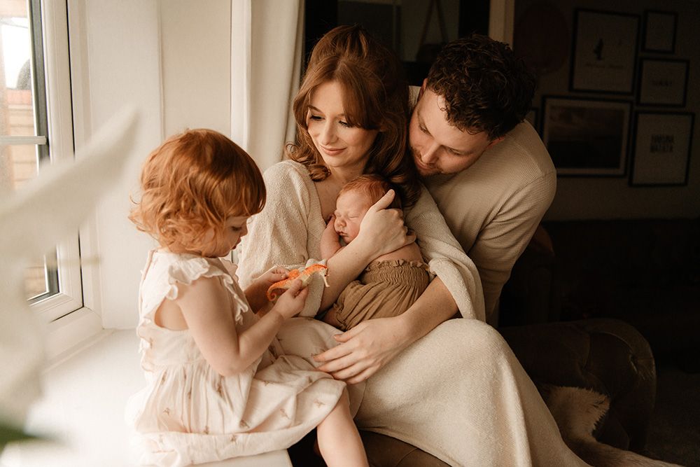 Family photoshoot in Lancashire. A family sits together by a bright window in their home, sharing an intimate moment in warm.