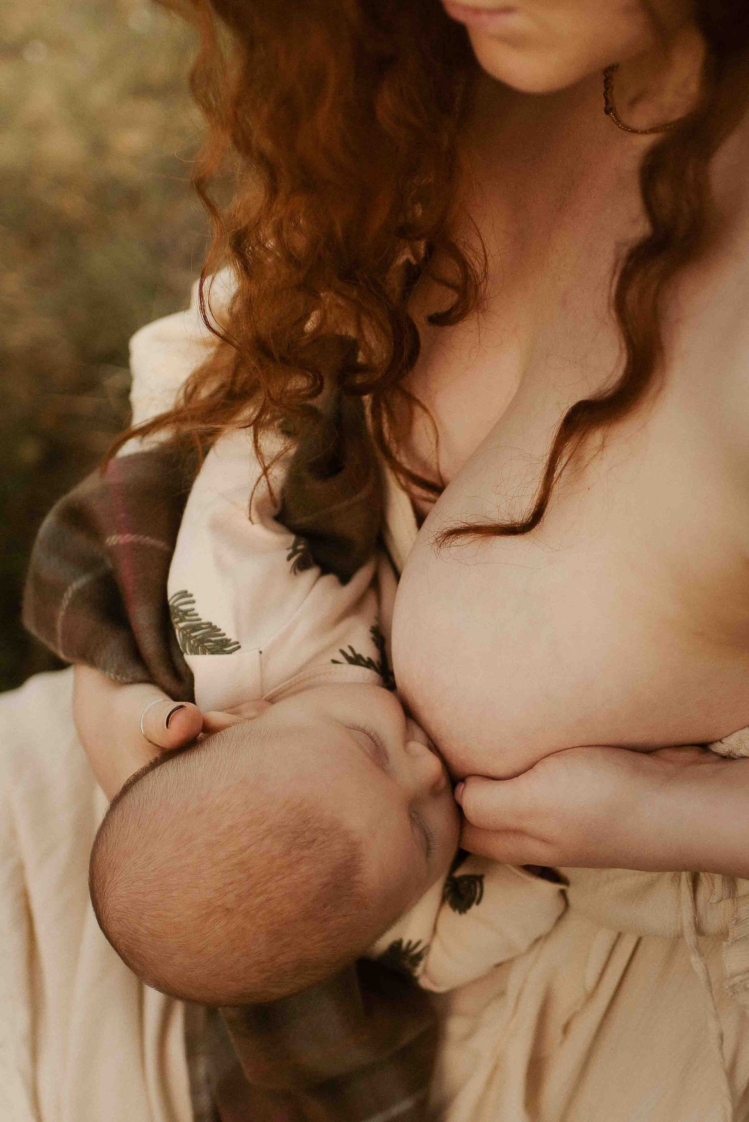Intimate close-up of mother in soft cream dress breastfeeding a baby with gentle natural lighting and curly hair.
