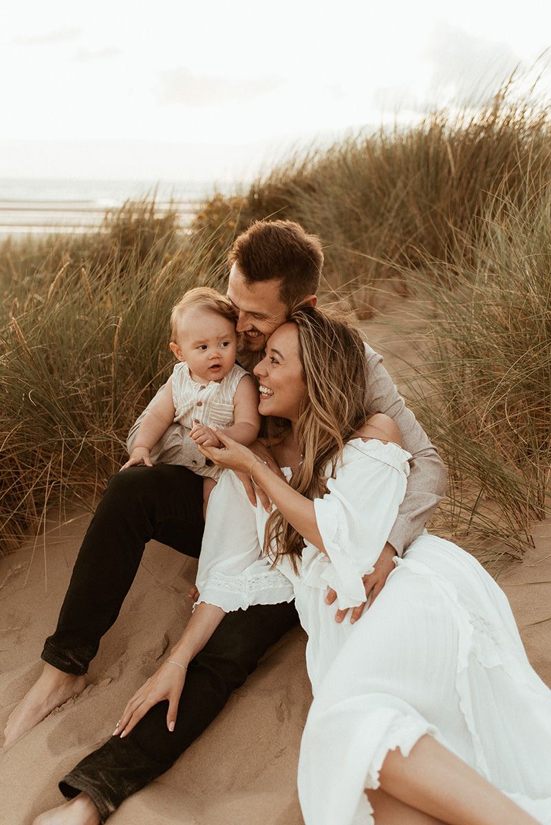 A family shares an intimate moment together while sitting on sandy dunes at sunset during Formby beach family photography session.
